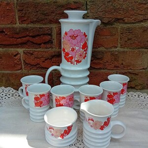 May include: A set of white ceramic teacups and teapot with a pink and red floral design. The set includes a teapot, creamer, sugar bowl, and six teacups.