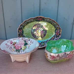 May include: Three decorative ceramic serving dishes. The largest is an oval platter with a green and gold floral design. A footed bowl features pink roses, and a smaller green bowl has a floral border.