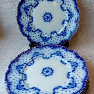 May include: A set of four blue and white porcelain dinner plates with a scalloped edge and a floral design. The plates are stacked on top of each other.