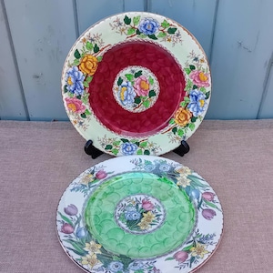 Puede incluir: Dos platos decorativos con diseños florales. Uno tiene un centro rojo con un patrón floral y un borde verde claro con flores coloridas. El otro tiene un centro verde y un borde blanco con flores y tulipanes.