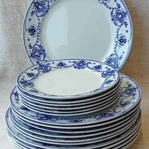 May include: A stack of 18 white ceramic dinner plates with a blue floral pattern around the rim.