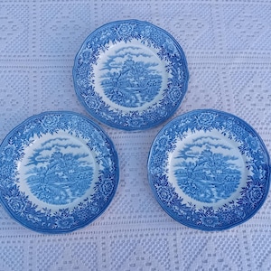 May include: Three blue and white porcelain plates with a cottage scene design. The plates have a scalloped edge and a floral pattern.