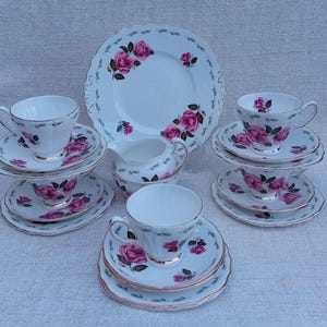 May include: A vintage tea set with a floral design. The set includes a teapot, creamer, sugar bowl, cups, and saucers. The floral design features pink roses and green leaves on a white background.