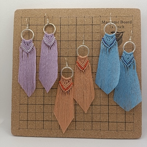 May include: Four pairs of macrame earrings with different colored tassels and silver hoops. The earrings are displayed on a cork board with a grid pattern. The text "Macrame Board 7xinch" is printed on the board.