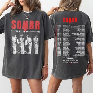 May include: Dark gray t-shirt featuring the band name "SOMBR" in red block letters above a black and white image of four band members. The back of the shirt lists tour dates and locations.