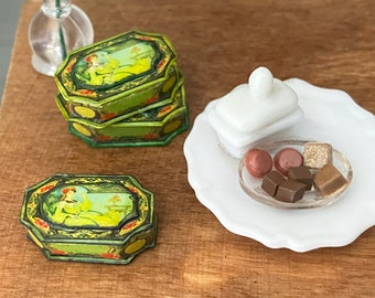 May include: Two vintage green and gold metal boxes with a woman in a dress on the lid. A white ceramic dish with a lid and a small clear dish with assorted chocolate candies.