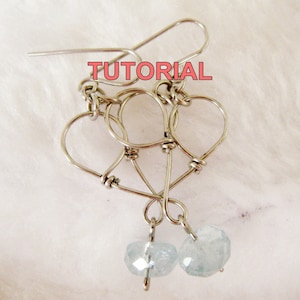 May include: Silver wire earrings with a heart design and light blue gemstone accents. The earrings are handmade and feature a delicate, intricate design.