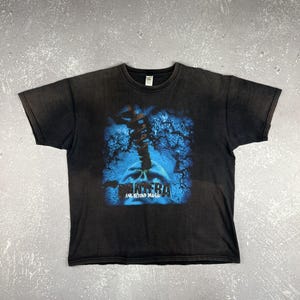 May include: Black t-shirt featuring a blue and white graphic design. The graphic includes a skull and the band name "PANTERA" with the text "FAR BEYOND DRIVEN". The shirt has a crew neck and short sleeves.