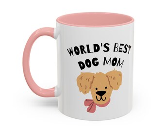 Könnte beinhalten: Weiße Keramik-Tasse mit rosa Innenraum und Henkel. Die Tasse zeigt den schwarzen Text "WORLD'S BEST DOG MOM" zusammen mit einer Cartoon-Illustration eines goldenen Hundes mit rosa Schleife.