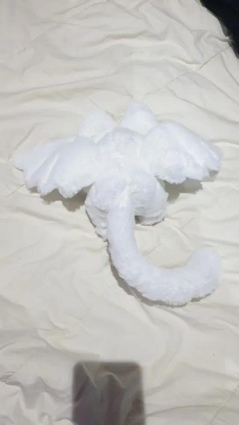 Puede incluir: Juguete de drag&oacute;n de peluche blanco con alas y una cola larga. El drag&oacute;n est&aacute; acostado de espaldas con las alas extendidas.