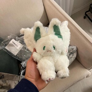 Puede incluir: Juguete de peluche blanco con orejas verdes y una cara triste. El juguete tiene una textura esponjosa y est&aacute; sosteniendo sus patas juntas.