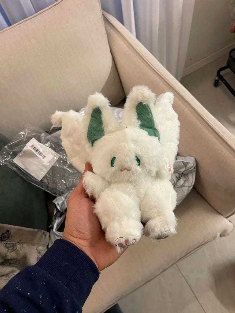 Puede incluir: Juguete de peluche blanco con orejas verdes y una cara triste. El juguete tiene una textura esponjosa y est&aacute; sosteniendo sus patas juntas.