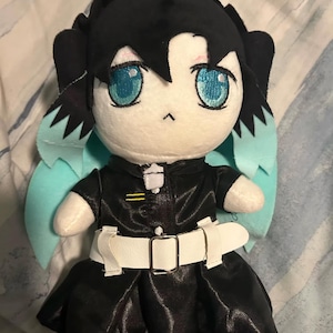 May include: A plush toy of a character with black hair, blue eyes, and a black and white outfit. The toy is wearing a white belt with a silver buckle. The toy has light blue wings.