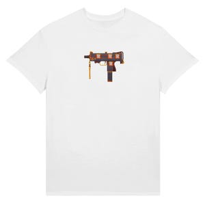 May include: White t-shirt featuring a graphic of a stylized submachine gun in black, orange, and gold. The design includes the letters "R" in orange. The shirt has a classic crew neck and short sleeves.