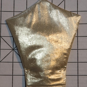 May include: Gold-colored, metallic fabric item with a unique shape. The item has a wide, flared base that tapers to a point at the top. The material has a shiny, textured appearance, suggesting a costume or decorative element.