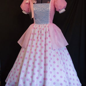May include: A pink and white polka dot dress with a pink lace bodice and a matching pink bonnet. The dress has a full skirt and a white lace trim.