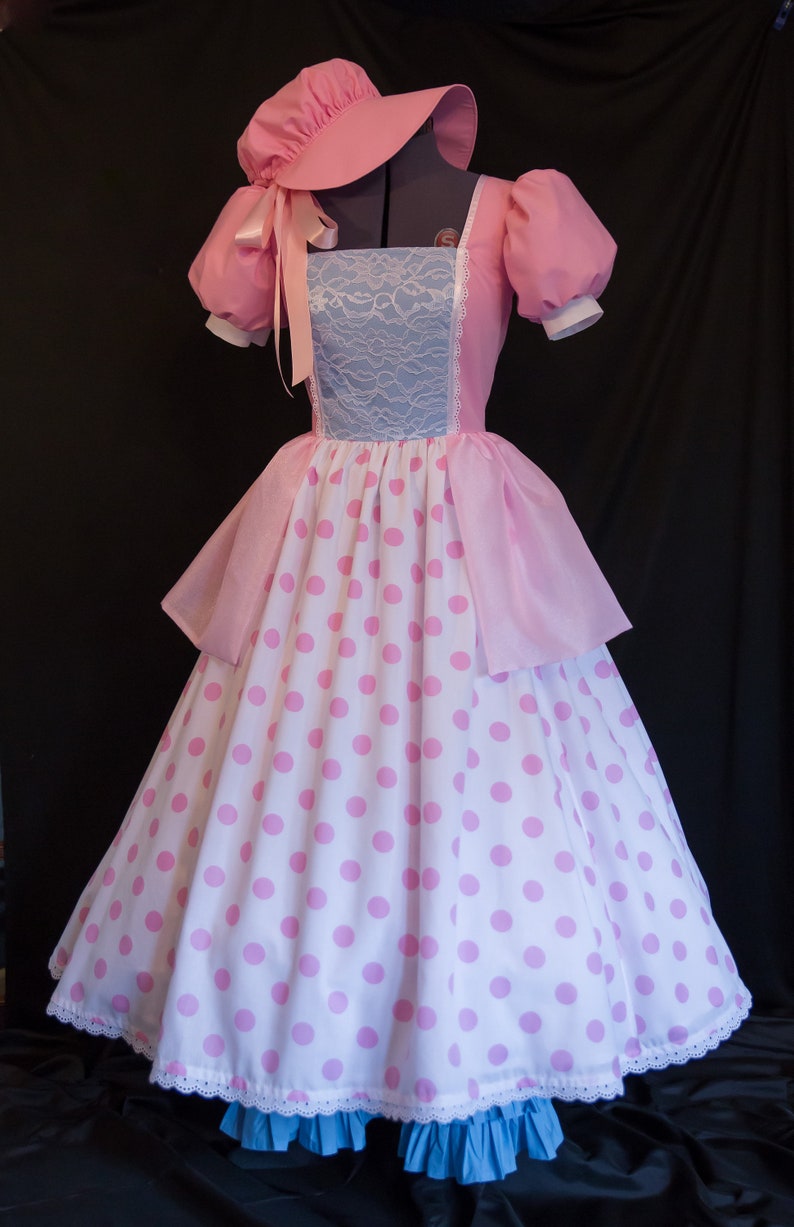 May include: A pink and white polka dot dress with a pink lace bodice and a matching pink bonnet. The dress has a full skirt and a white lace trim.