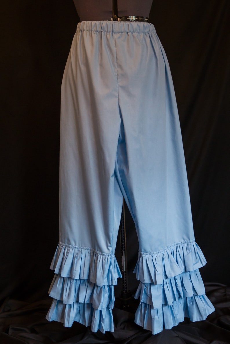 May include: Light blue cotton bloomers with multiple layers of ruffles at the bottom. The bloomers have an elastic waistband.