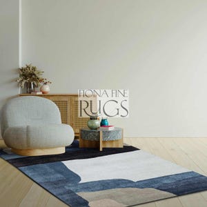 Peut inclure: Tapis moderne avec un motif abstrait. Le tapis présente une palette de couleurs de bleu, blanc et gris, avec une bordure noire. Le texte "FIONA FINE RUGS" est visible. Le tapis est dans un salon avec un fauteuil et une petite table.