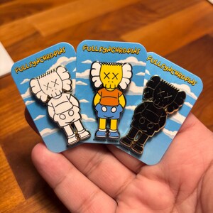 Pode incluir: Tr&ecirc;s pinos de esmalte com personagens de desenhos animados com olhos em forma de X. Um &eacute; branco, outro preto e outro amarelo com uma camisa laranja e cal&ccedil;&otilde;es azuis. Cada pino est&aacute; em um cart&atilde;o azul com o texto "FULLSYNCHROPINS".