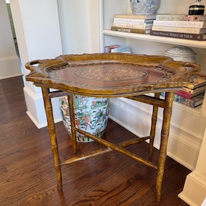 May include: A decorative wooden serving tray with a bamboo-style stand. The tray has a dark brown border and a central design with gold and red accents. The stand is made of bamboo-style wood. The tray is approximately 28 inches long.
