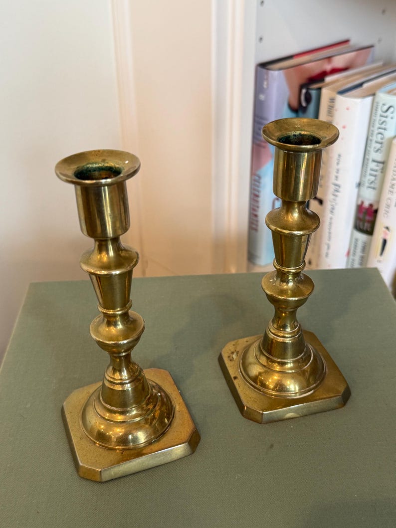 Puede incluir: Dos candelabros antiguos de lat&oacute;n. Cada candelabro tiene una base cuadrada, un tallo decorativo y una parte superior circular para sostener una vela. El lat&oacute;n tiene un tono dorado c&aacute;lido y el dise&ntilde;o es cl&aacute;sico y elegante.