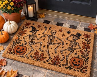 May include: A rectangular coir doormat featuring a printed design of three dancing skeletons surrounded by orange pumpkins, autumn leaves, and small stars. The skeletons are depicted in various poses, with one wearing a witch hat and another a top hat.