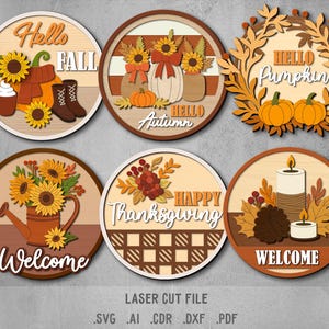 May include: A selection of laser-cut wooden decorations with autumnal themes. The circular designs feature pumpkins, sunflowers, and candles, with phrases like "Hello Fall," "Hello Autumn," and "Welcome." The colour palette includes brown, orange, and cream.