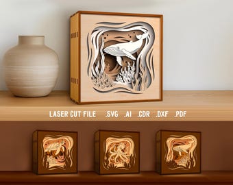 May include: A wooden laser-cut light box featuring a whale design. The layered artwork depicts a whale swimming in the ocean, with coral and other sea life. The text "LASER CUT FILE .SVG .AI .CDR .DXF .PDF" is visible.