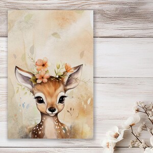 Könnte beinhalten: Ein Aquarellbild eines Rehs mit einer Blumenkrone. Das Reh hat braunes Fell und große, dunkle Augen. Der Hintergrund ist in einem sanften Pfirsichton mit Aquarell-Waschungen gehalten.