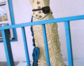 May include: A white corset with a brown belt and a small pouch, worn over a cream-colored skirt with ruffles. The skirt has a blue sash tied at the waist. The outfit is displayed on a mannequin against a white wall.