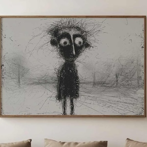 May include: A black and white abstract drawing of a person with a large head and exaggerated features hangs on a white wall above a light brown sofa with pillows. The sofa is in a living room with a vase of dried pampas grass on the right side of the image.