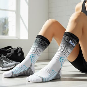 Könnte beinhalten: Weiße Sportsocken mit schwarzen und grauen Akzenten und blauen Details. Die Socken haben ein Farbverlaufsdesign und das Wort "Jenna" ist auf der Seite aufgedruckt. Die Socken sind kniehoch und scheinen aus atmungsaktivem Material zu sein.