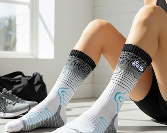 May include: White athletic socks with black and grey accents and blue detailing. The socks have a gradient design and the word "Jenna" is printed on the side. The socks are knee-high and appear to be made of a breathable material.