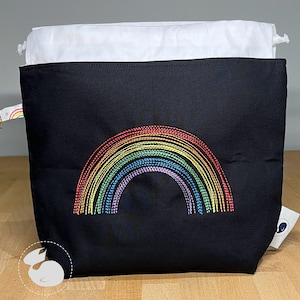 May include: Black fabric pouch with a white lining and a rainbow embroidered design. The rainbow is made of multi-colored thread.