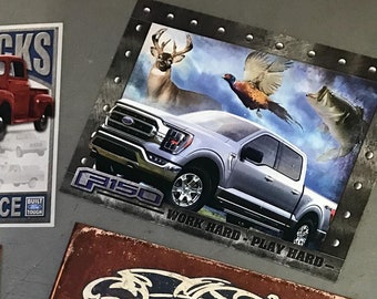 Op de afbeelding: Een verzameling vintage metalen borden met Ford-trucks, -auto's en -logo's. De borden zijn in verschillende kleuren en hebben verschillende ontwerpen, waaronder een rode Ford F-Series-truck, een blauwe Ford Mustang en een zwart-wit Ford-logo.