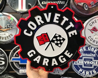 Könnte beinhalten: Ein zahnradförmiges Metallschild mit schwarzem Hintergrund und rotem Rand. Der Text CORVETTE GARAGE ist in Weiß gedruckt, zentriert über und unter einer Grafik einer roten Flagge mit einer Lilie und einer schwarz-weiß karierten Flagge.