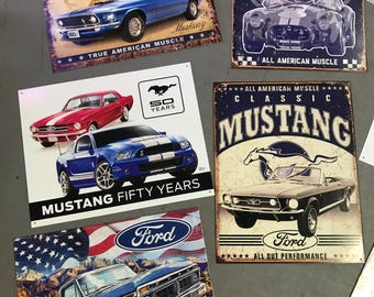 Könnte beinhalten: Eine Sammlung von Vintage-Blechschildern mit Ford Mustang und Shelby Cobra Autos. Die Schilder sind mit amerikanischer Flaggen-Symbolik und den Worten "True American Muscle", "All American Muscle", "Classic Mustang", "Mustang Fifty Years", "Driven by Freedom" und "All Out Performance" verziert.