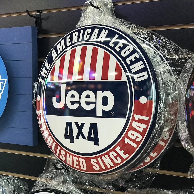 Puede incluir: Un letrero redondo de metal con un dise&ntilde;o rojo, blanco y azul. El letrero dice "The American Legend Jeep 4x4 Established Since 1941".
