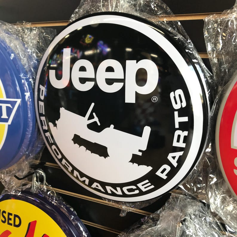 Puede incluir: Un letrero redondo de metal negro y blanco con el texto "Jeep Performance Parts" en un c&iacute;rculo alrededor de una silueta de un Jeep. El letrero tiene un fondo negro y letras blancas.