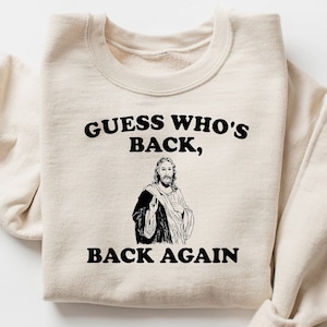 May include: A beige sweatshirt with the text "GUESS WHO'S BACK, BACK AGAIN" and a black and white illustration of Jesus.