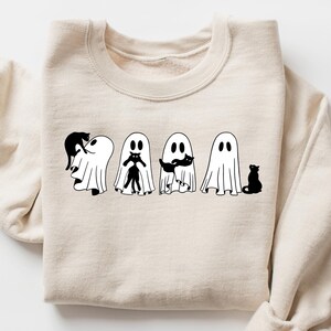 May include: A beige sweatshirt with a black and white graphic of four ghosts and a black cat. The ghosts are holding black cats in their arms.