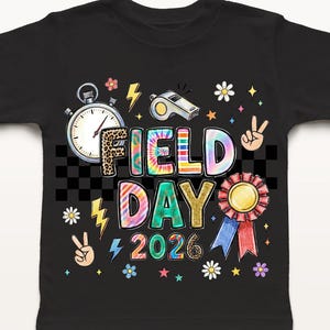 May include: Black t-shirt featuring a colourful "FIELD DAY 2026" graphic. The design includes a stopwatch, whistle, peace signs, flowers, and a ribbon. The letters in "FIELD DAY" are tie-dye.