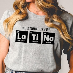 May include: A gray t-shirt with a black graphic of the periodic table elements La, Ti, and Na. The text above the graphic reads "The Essential Element".
