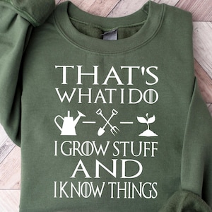 May include: Green sweatshirt with white text that reads "That's what I do I grow stuff and I know things". The text is accompanied by a gardening-themed graphic with a watering can, a shovel, and a sprout.