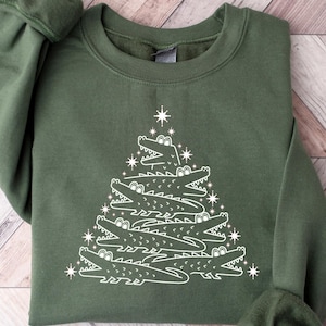 May include: A green sweatshirt with a white design of a Christmas tree made of alligators. The tree is decorated with stars.