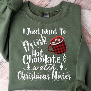 May include: Green sweatshirt with the text "I Just Want To Drink Hot Chocolate & Watch Christmas Movies." A red and black plaid mug of hot chocolate is featured in the design. The sweatshirt has a crew neck and long sleeves.
