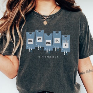 May include: A dark gray t-shirt with a graphic of five IV bags, each labeled with a medical abbreviation. The text "#FIFTHPRESSOR" is printed below the graphic.
