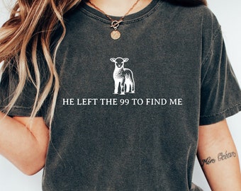 May include: A dark gray t-shirt with a white graphic of a lamb and the text "He left the 99 to find me".