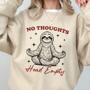 May include: A beige sweatshirt with a graphic of a meditating sloth and the text "NO THOUGHTS HEAD EMPTY".